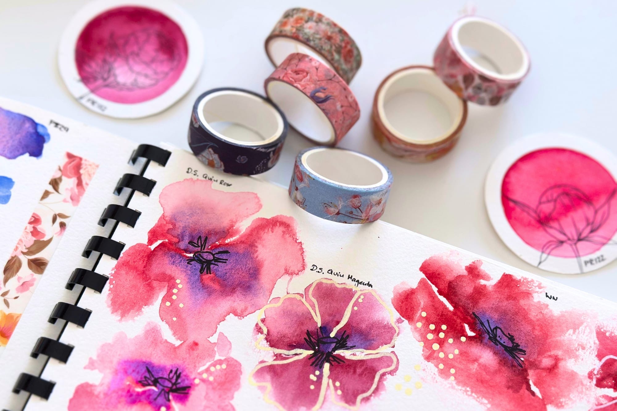 Florale Washi-Tape-Rollen neben Aquarellskizzen im Skizzenbuch